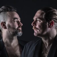 Die beiden Musiker der Band Äffchen & Craigs in schwarzen Anzügen vor einer schwarzen Wand.