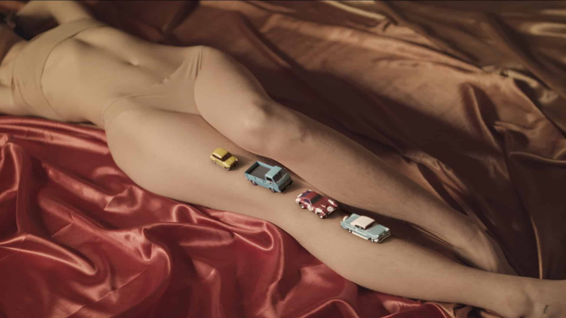 Videostill aus dem Musikvideo "Ella". Eine animierte Auto-Karawane fährt über das Bein einer nackten Frau.