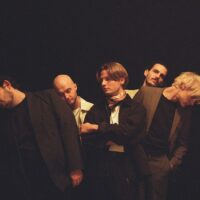 Ein dunkles Bild der Band Catastrophe & Cure mit einer gelblichen Belichtung mit schwarzem Hintergrund