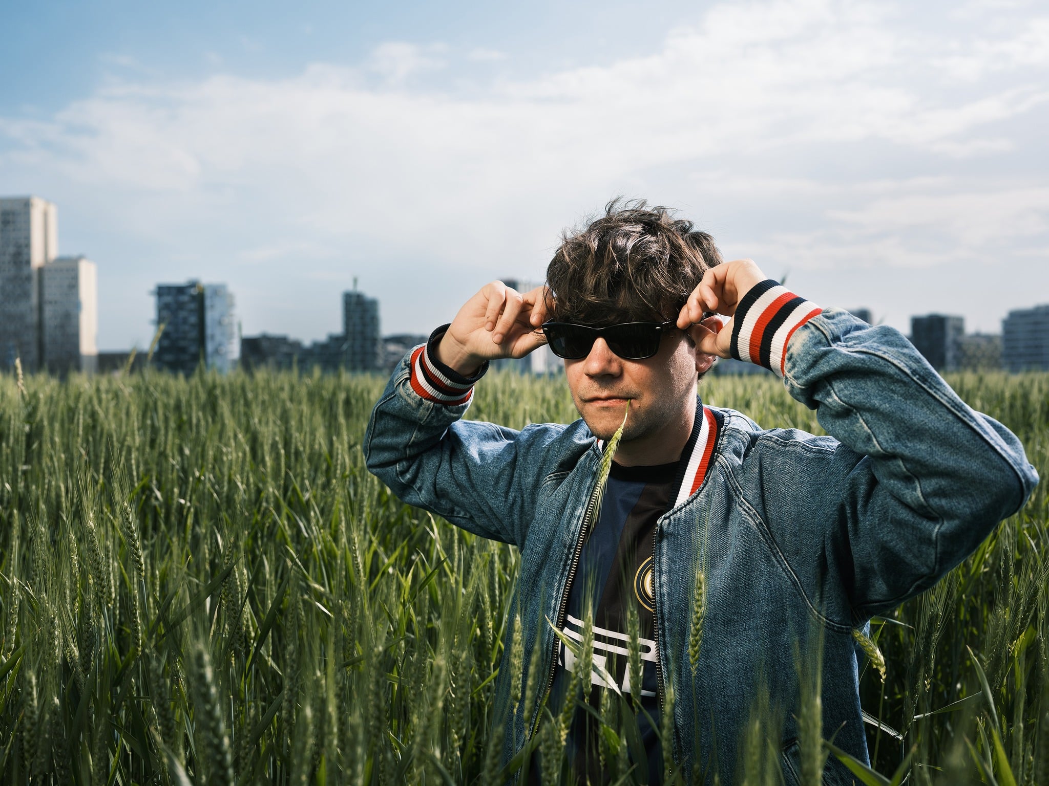 Der Liedermacher Der Nino aus Wien in einem grünen Weizenfeld vor der Skyline von Wien