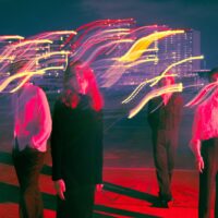 Bild der Band Die Wallners auf Platz vor Hochhäusern in rotem Licht beleuchtet