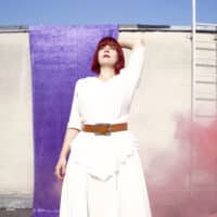Die Singer-Songwriterin Flickentanz in einem weißen Kleid, umgeben von rosa Rauch