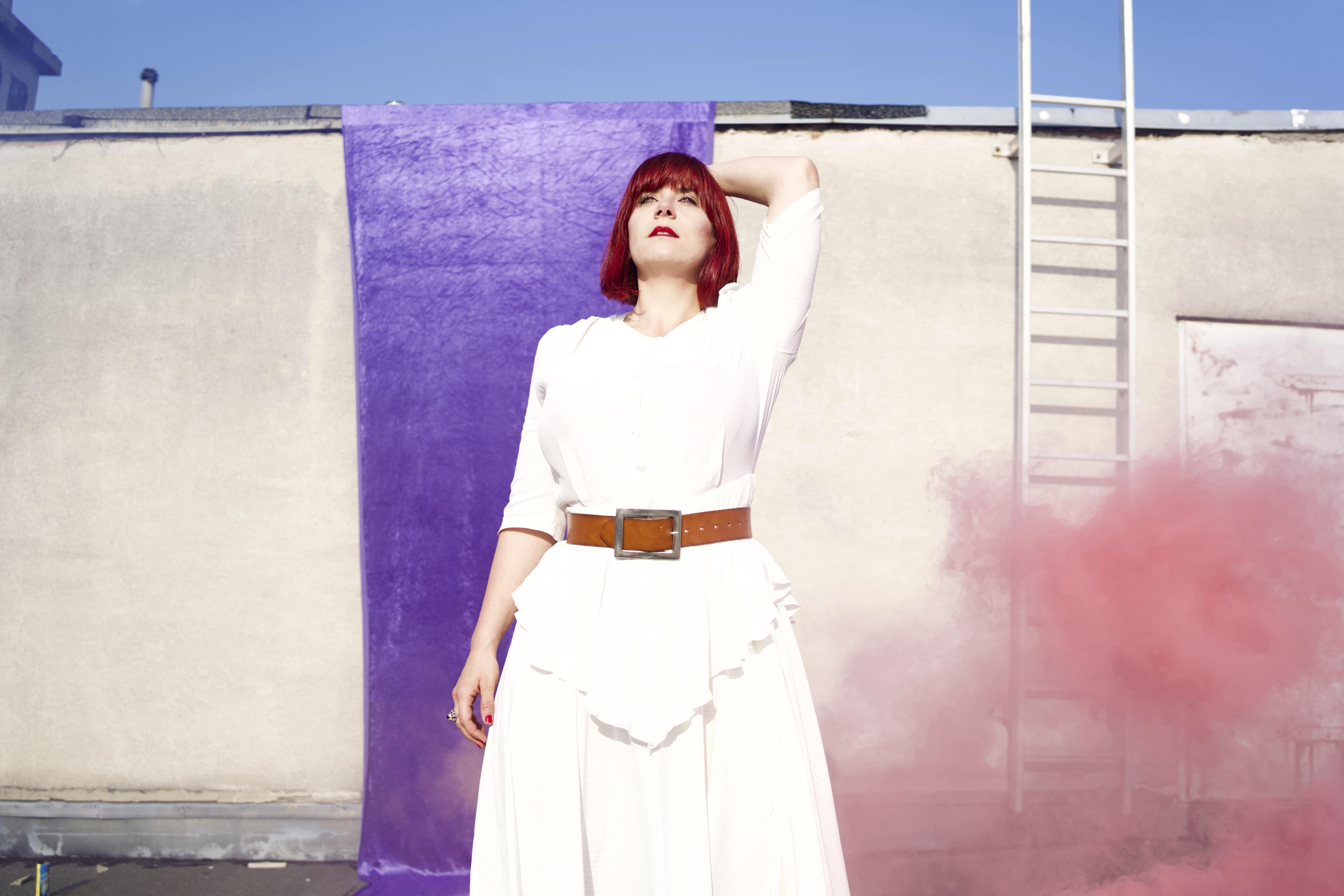 Die Singer-Songwriterin Flickentanz in einem weißen Kleid, umgeben von rosa Rauch