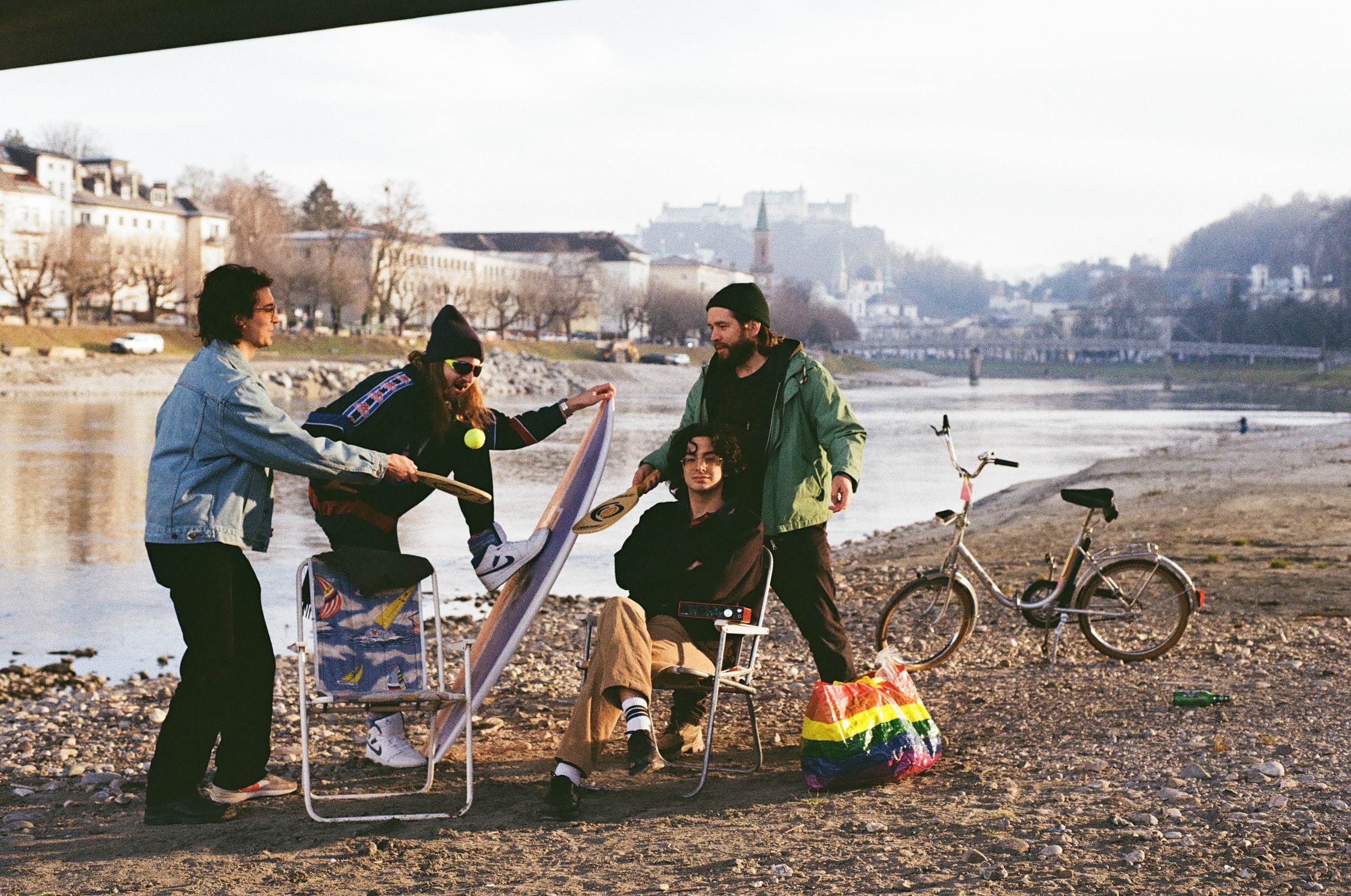 Die vierköpfige Band Flirtmachine am Ufer der Salzach, im Hintergrund die Stadt Salzburg und die Festung Hohensalzburg