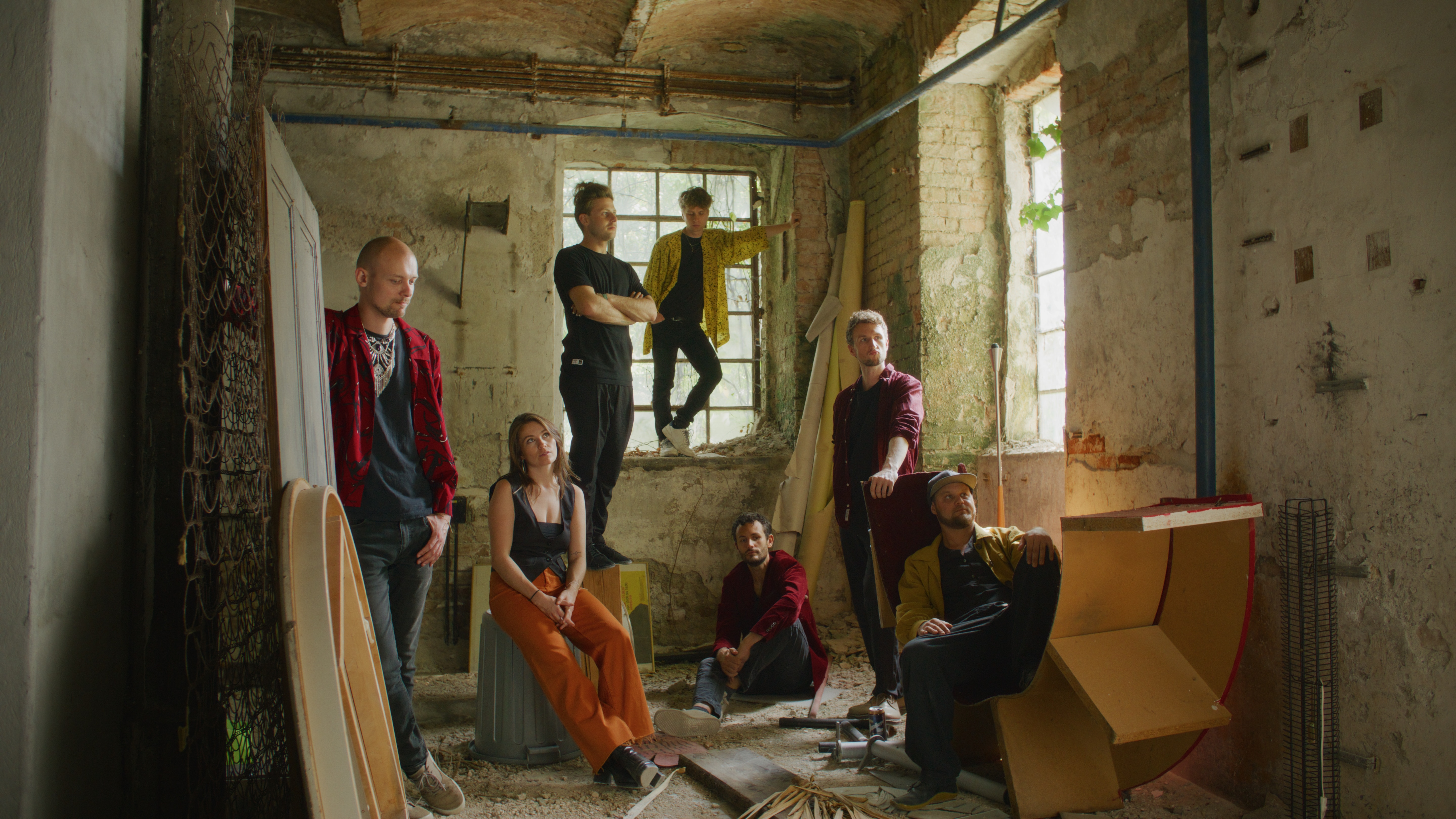 Die sechsköpfige Band GOT'YA in einem verlassenen Gebäude. Teilweise stehen die Mitglieder, teilweise sitzen sie.