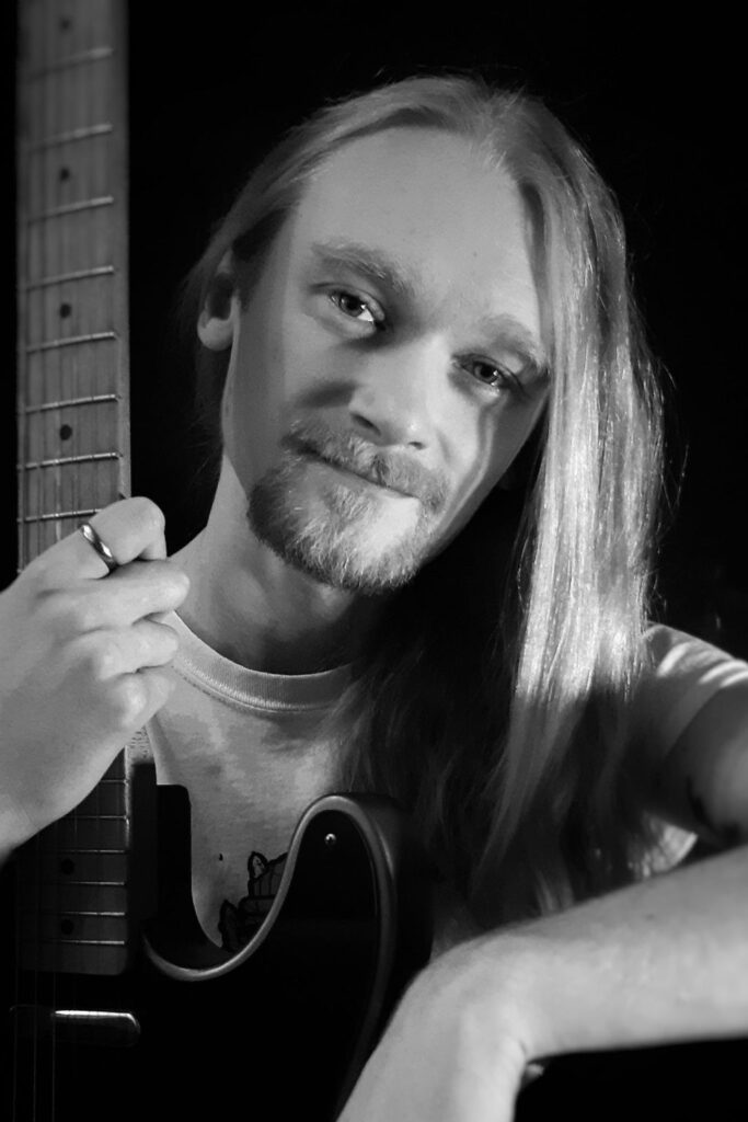 Ein schwarz-weiß-Bild des Musikers Güne Mocn mit einer Gitarre in der Hand.