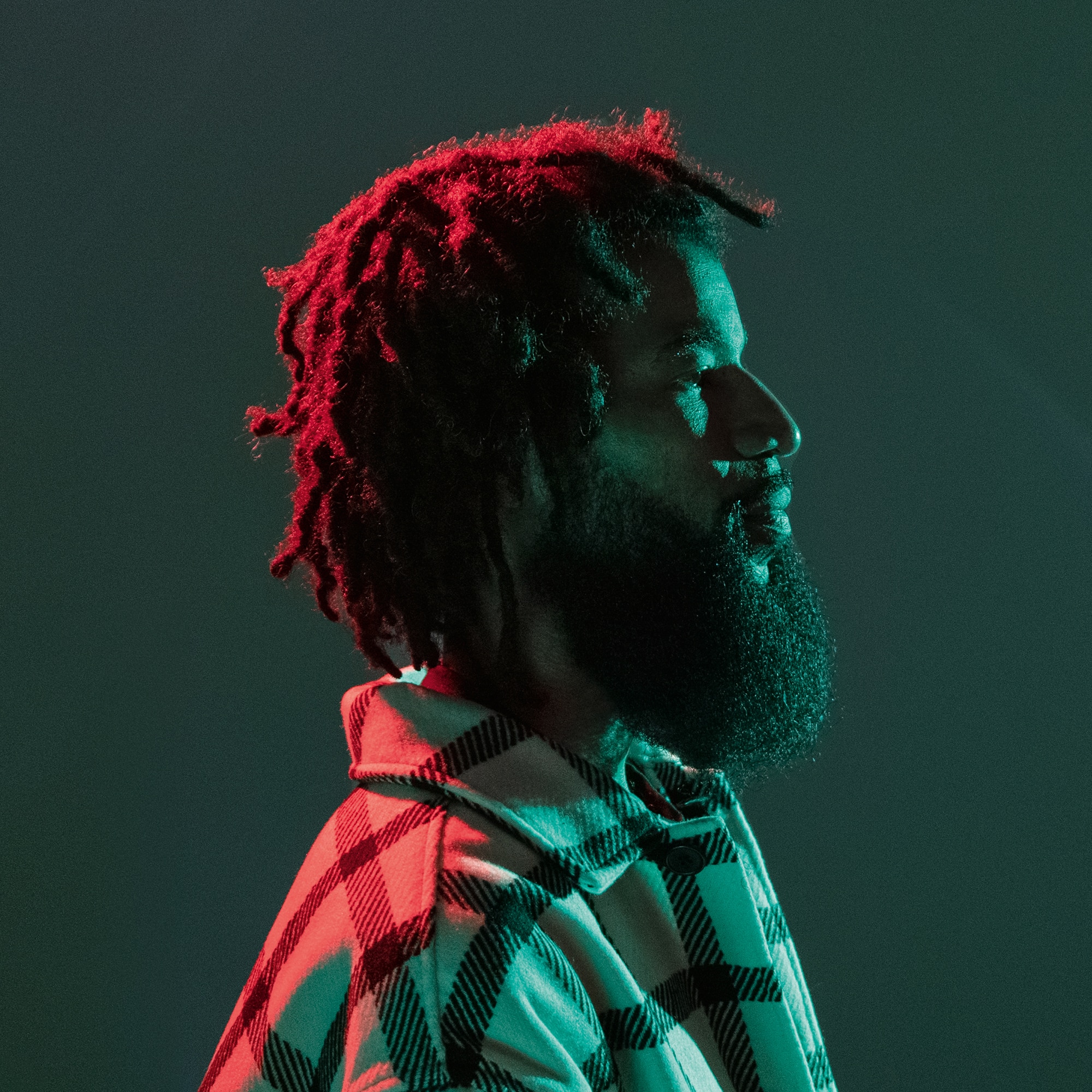 Der Künstler Jahson The Scientist im Seitenprofil vor einer grünen Wand beleuchtet mit roter und grüner Farbe