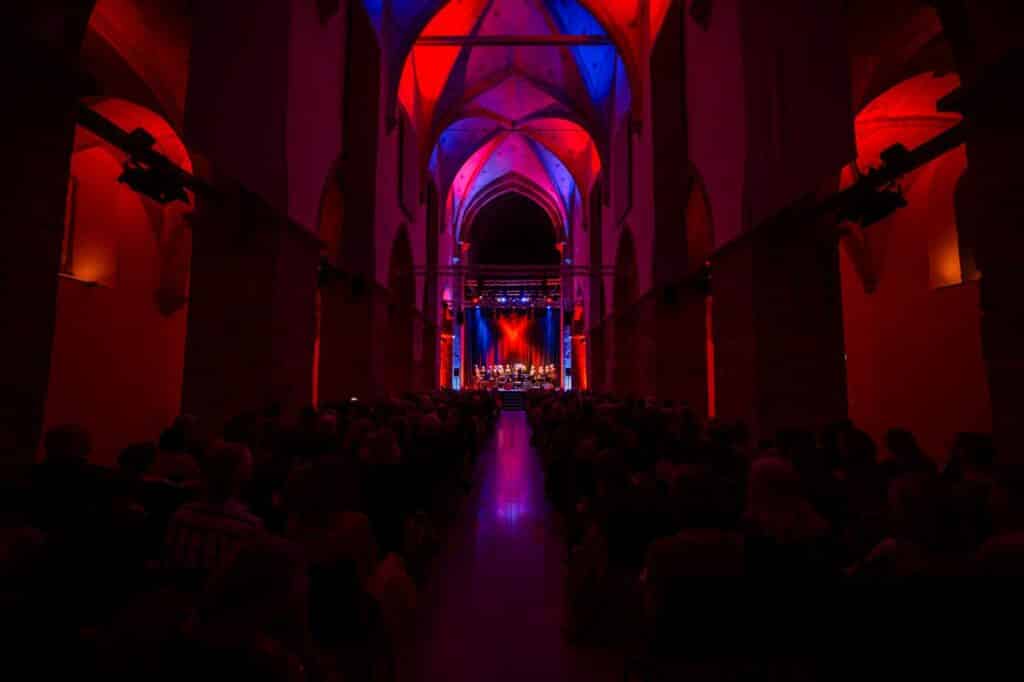 Bild des Innenraumes der Minoritenkirche während eines Konzertes, im roten Licht erleuchtet, von hinten fotografiert