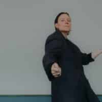 Ein Bild von Lan Rex in einem schwarzen Anzug vor einem hellblauen Hintergrund.