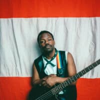 Der österreichische Musiker Mwita Mataro vor einer österreichischen Flagge mit einem schwarzen Bass in der Hand