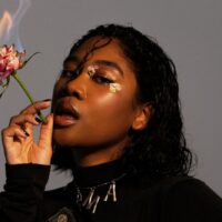 Ein Bild der Sängerin Rose May Alaba mit einer brennenden Rose in der Hand