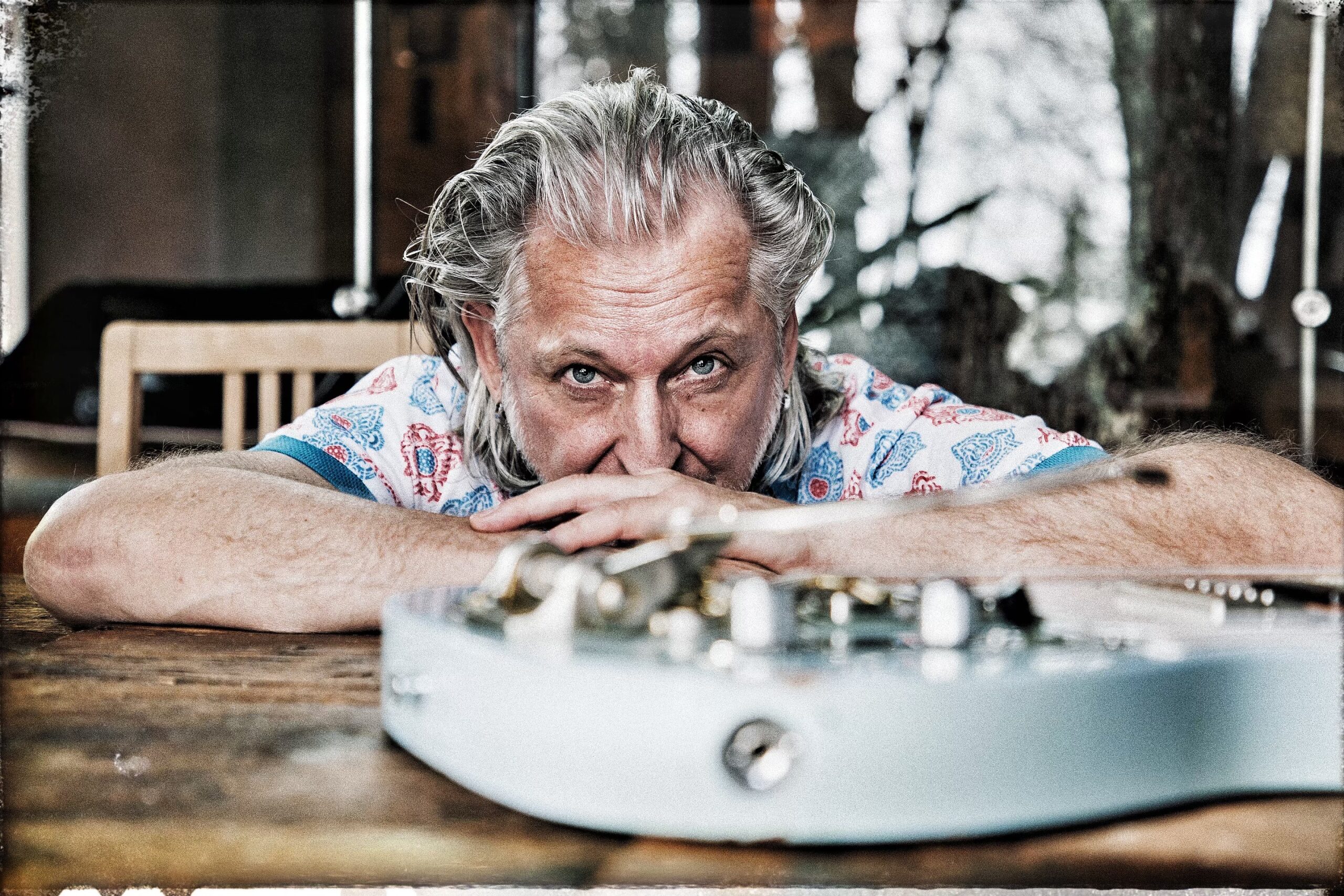 Bild Sir Oliver Mally am Tisch nach vorne lehnend mit einer Gitarre vor ihm liegend