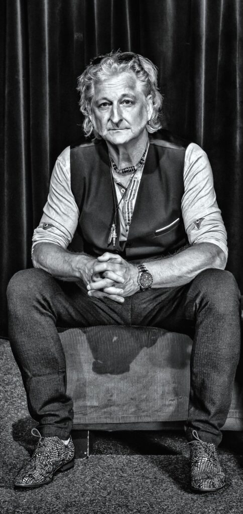 Sir Oliver Mally auf Zimmerstuhl nachvorne gelehnt sitzend