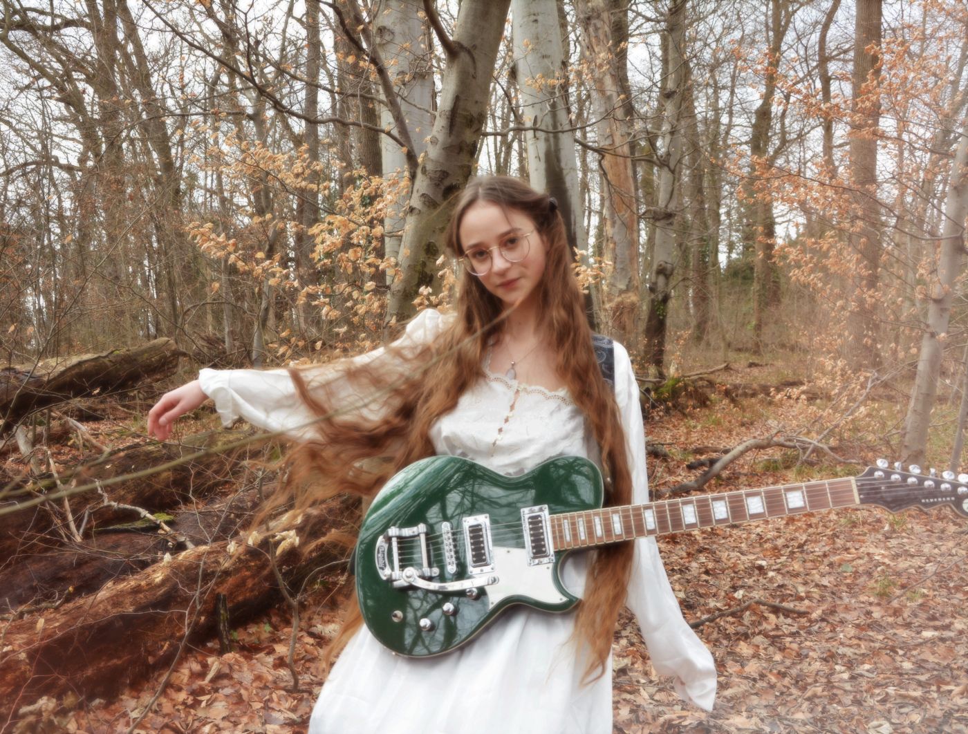 Bild der Liedermacherin Sodl in weißem Kleid im Wald mit Gitarre stehend