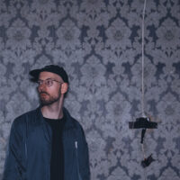 Der Musiker Willibald Schneider vor einer kaputten Tapettenwand.