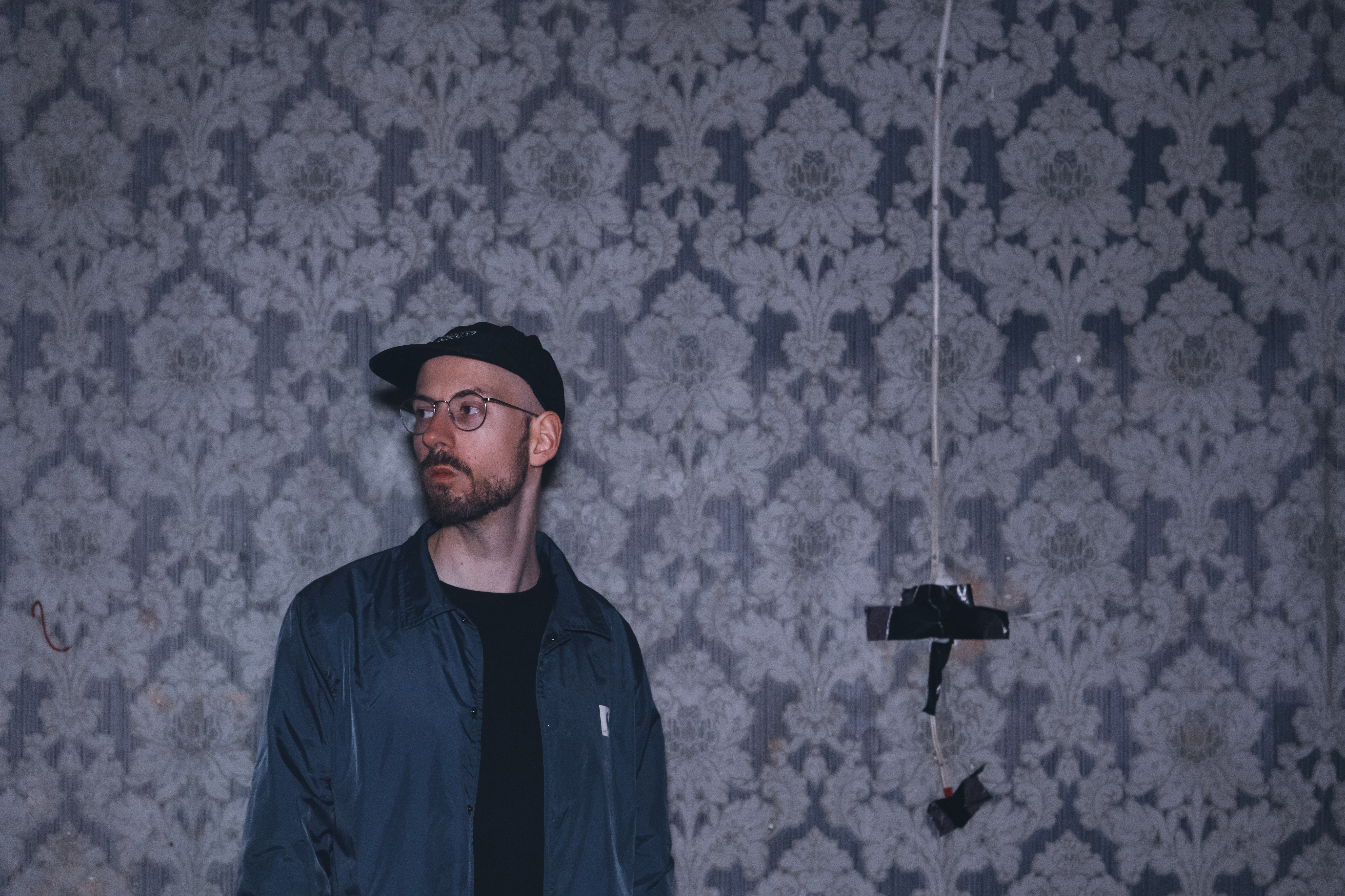 Der Musiker Willibald Schneider vor einer kaputten Tapettenwand.