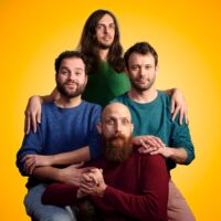 Die vierköpfige Band ZAPP GALURA vor einem gelben Hintergrund.