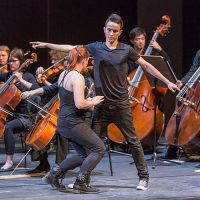 Zwei TänzerInnen vor den Celli eines Orchesters
