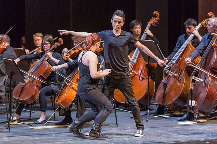 Zwei TänzerInnen vor den Celli eines Orchesters