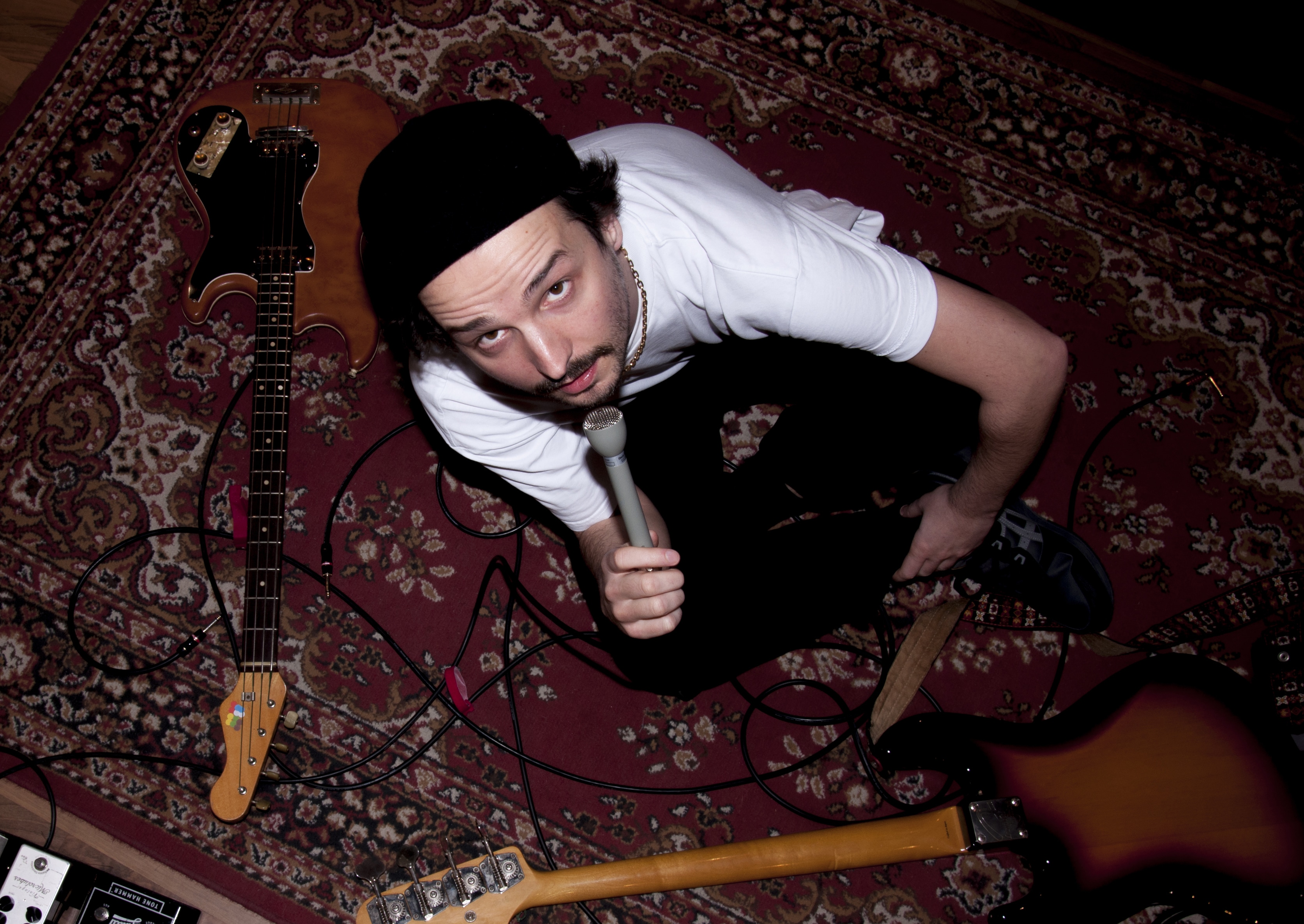 Der Musiker rossvanboss sitzt mit Bassgitarren und einem Mikrofon am Boden.