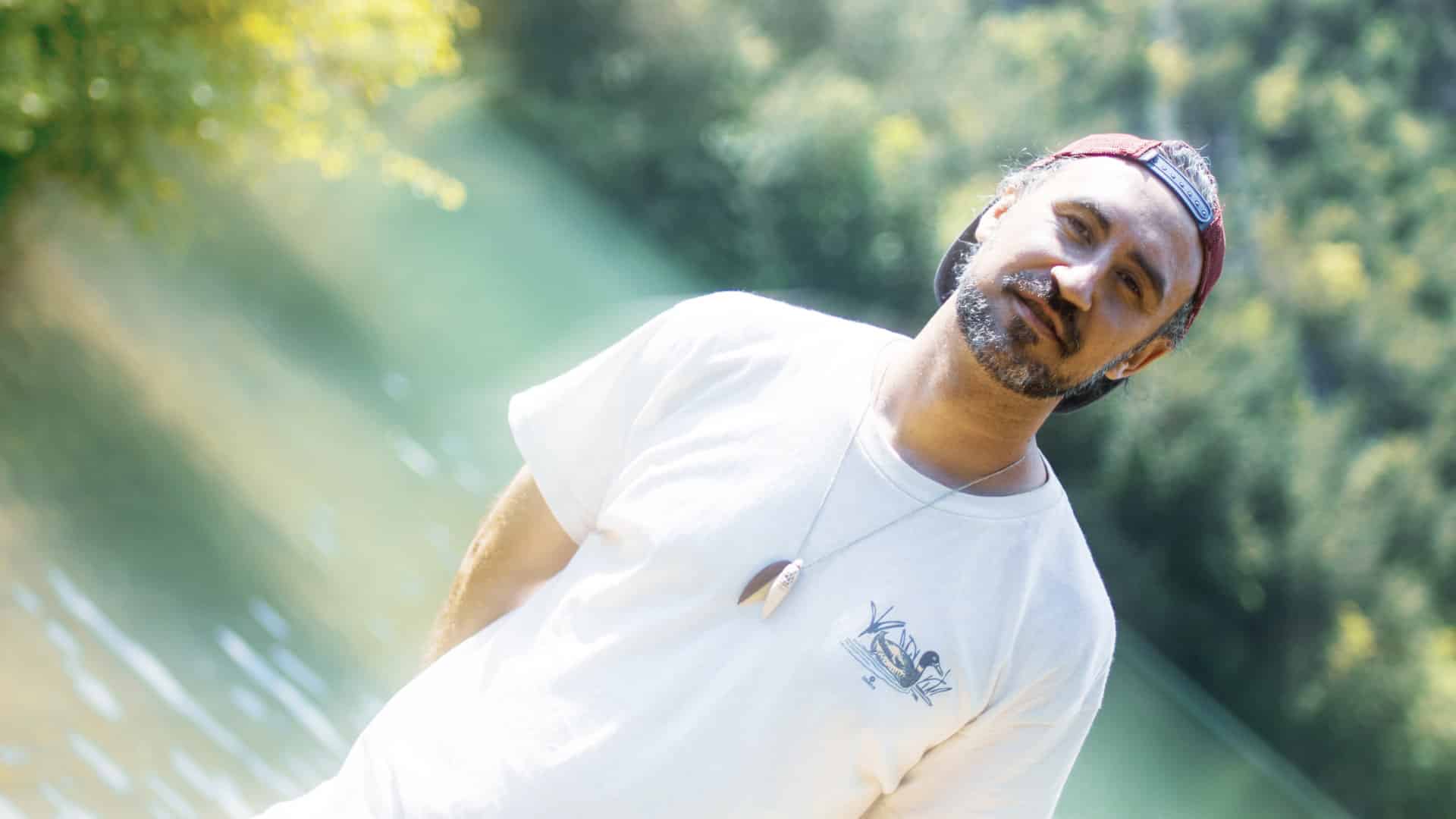 Der Singer-Songwriter trottoirs in einem weißen T-Shirt und roter, umgedrehter Kappe, vor einem grün-blauen Gewässer